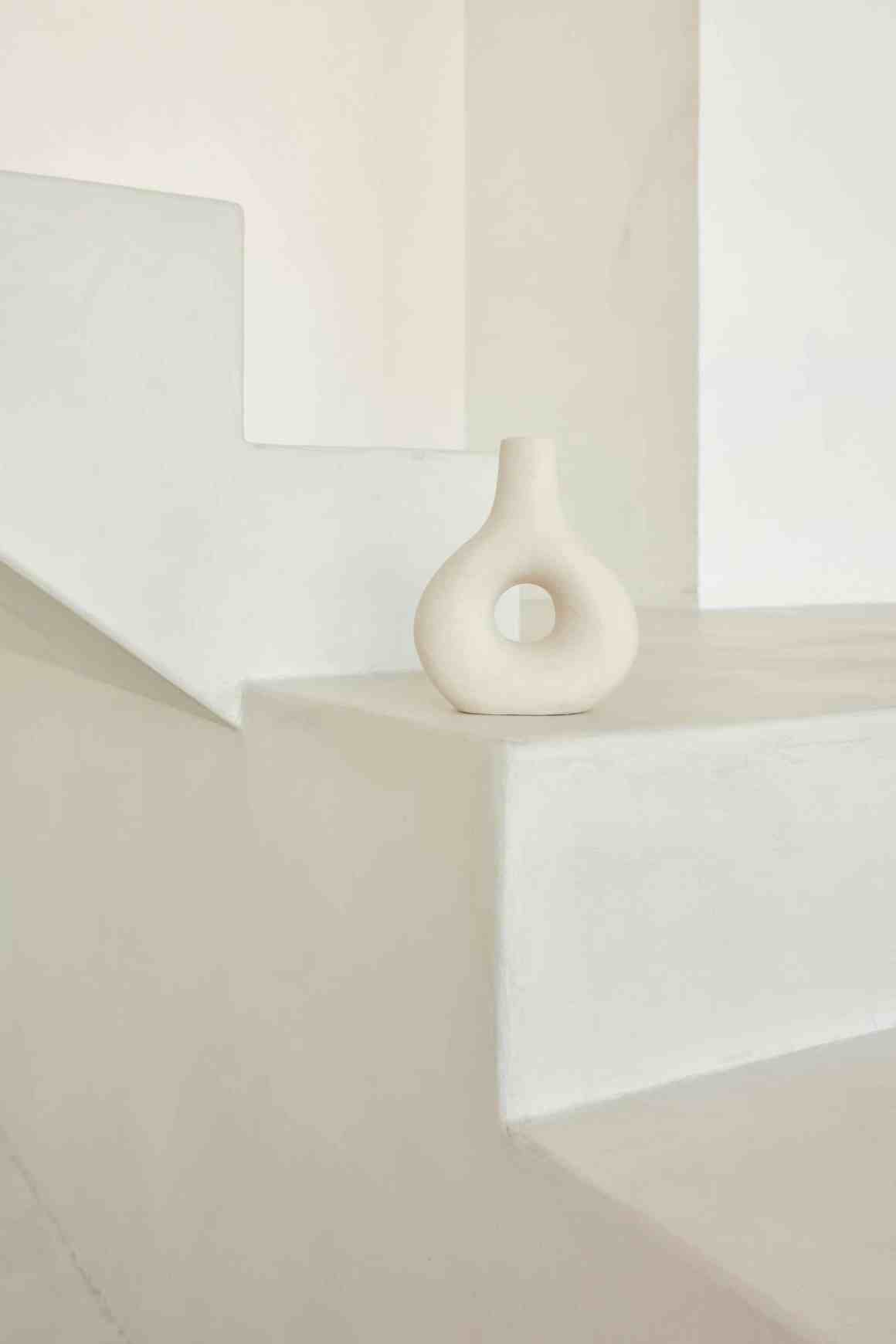 A minimalist room featuring a smooth, white surface with a sculptural vase on a staircase.
