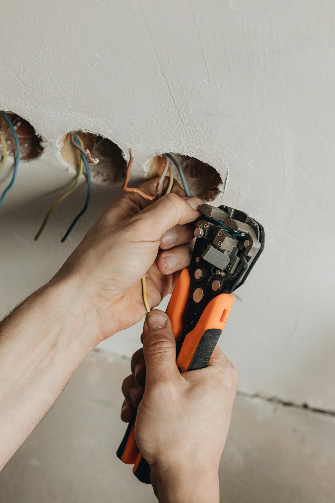 A person using wire strippers to prepare electrical wires coming from a wall, highlighting an electrical retrofitting process.