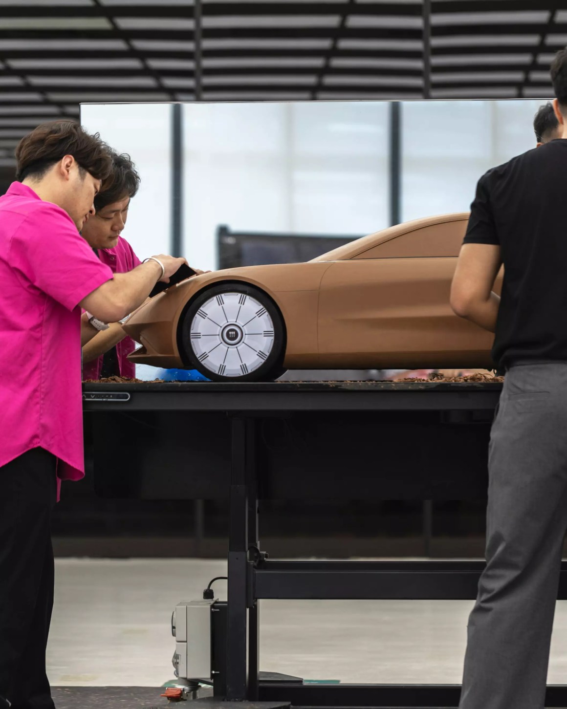 Two designers working on a clay model of a car in a design studio, with a sleek automotive design on display.