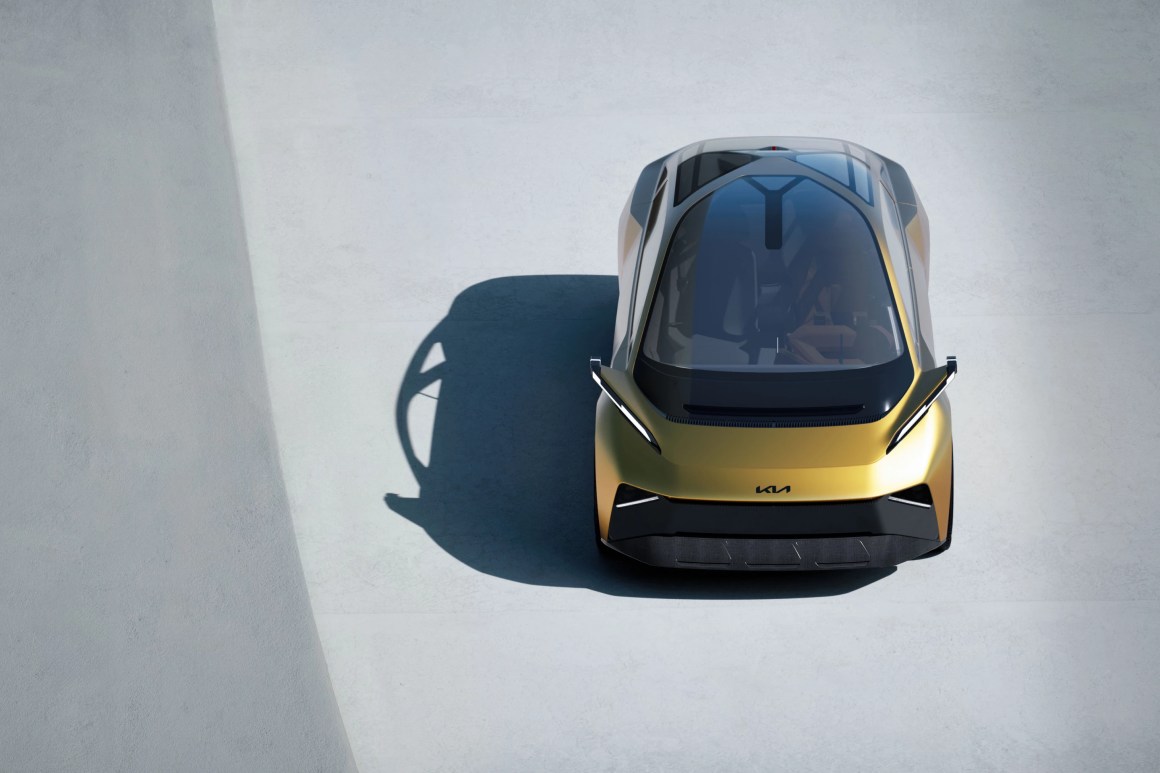 Aerial view of a modern concept car with a sleek, golden exterior and a futuristic design, parked on a light-colored surface.