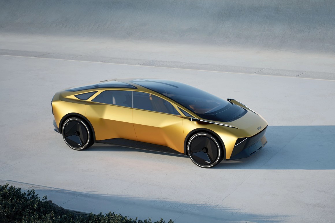 A futuristic concept car with a sleek golden exterior and large black wheels, showcased in a minimalistic outdoor setting.