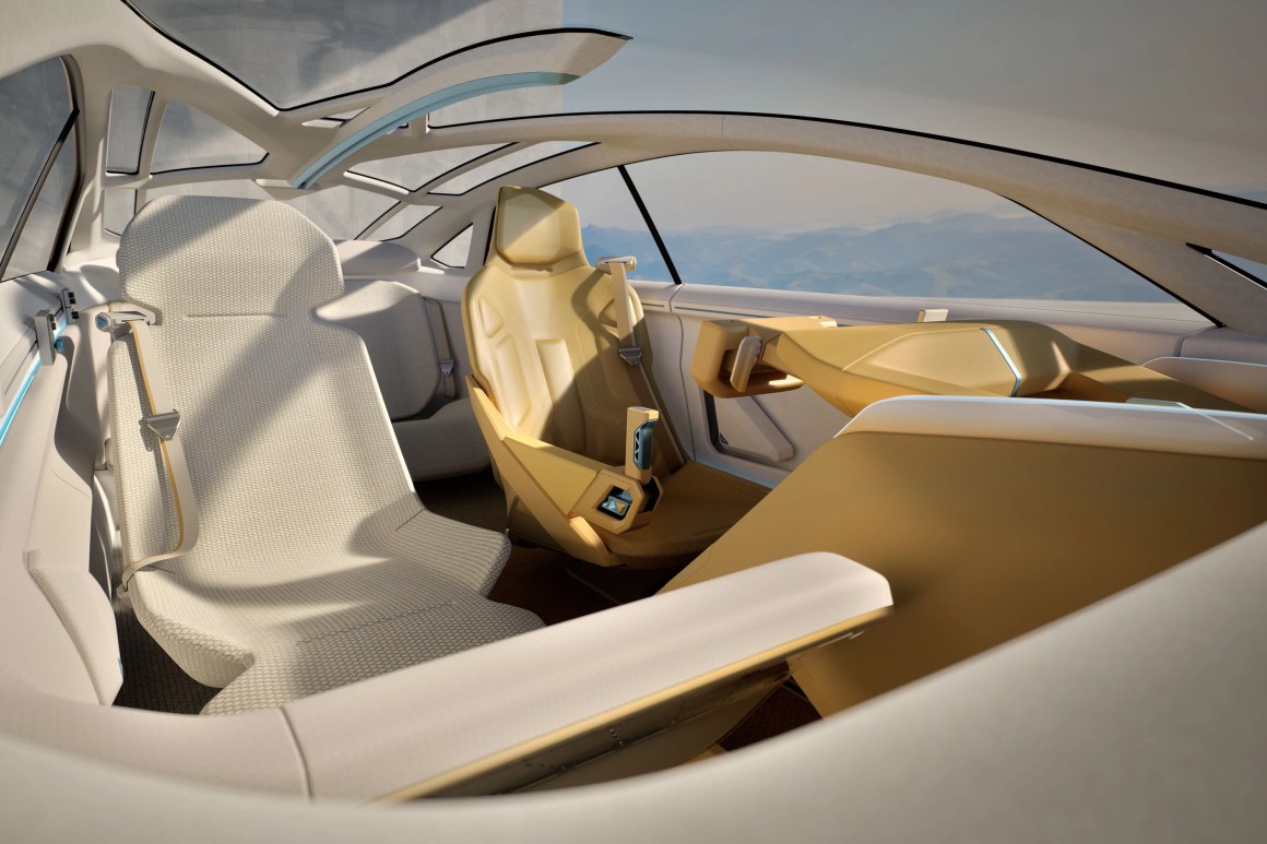 A futuristic car interior featuring two distinct seats, one in a beige fabric and the other in a striking yellow color. The design includes a sleek dashboard and panoramic windows, emphasizing a modern and spacious aesthetic.