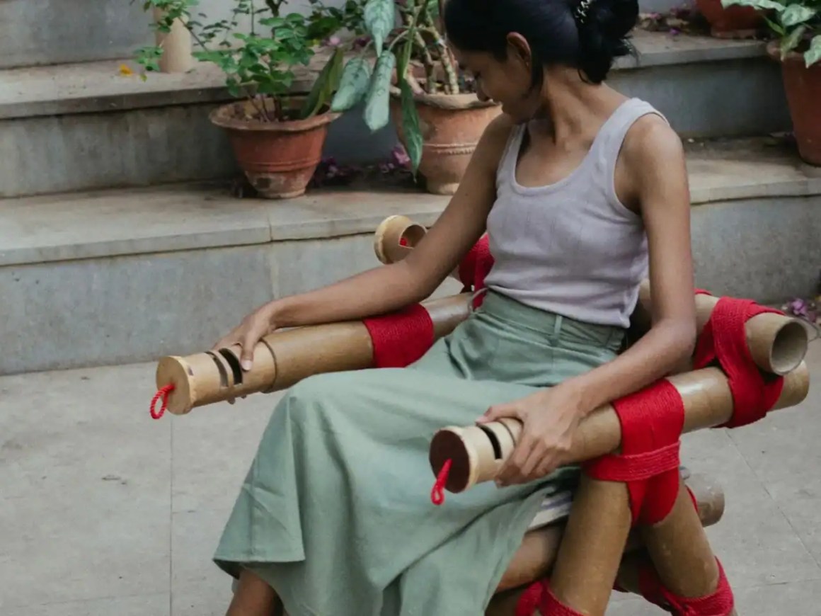 A woman sitting on a uniquely designed chair made of tubular materials and red ropes, surrounded by potted plants and steps.