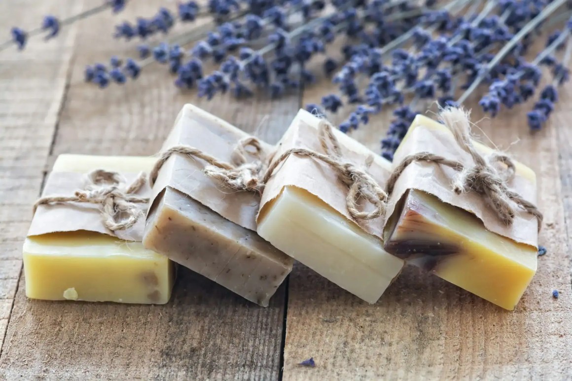 Four bars of natural handmade soap tied with twine, placed on a wooden surface with dried lavender in the background.
