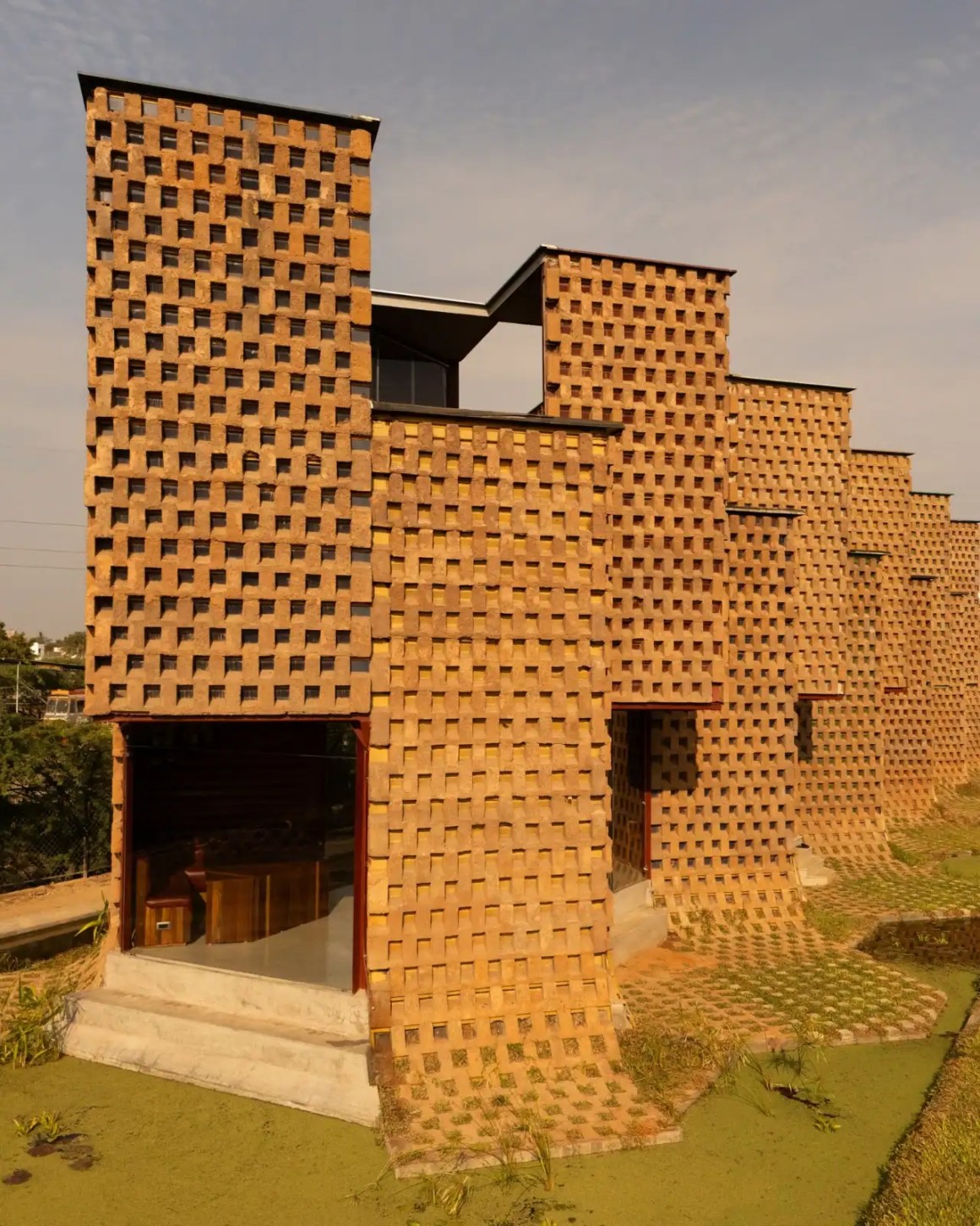 An artistic modern building featuring textured brick walls with a unique pattern, set against a natural landscape.