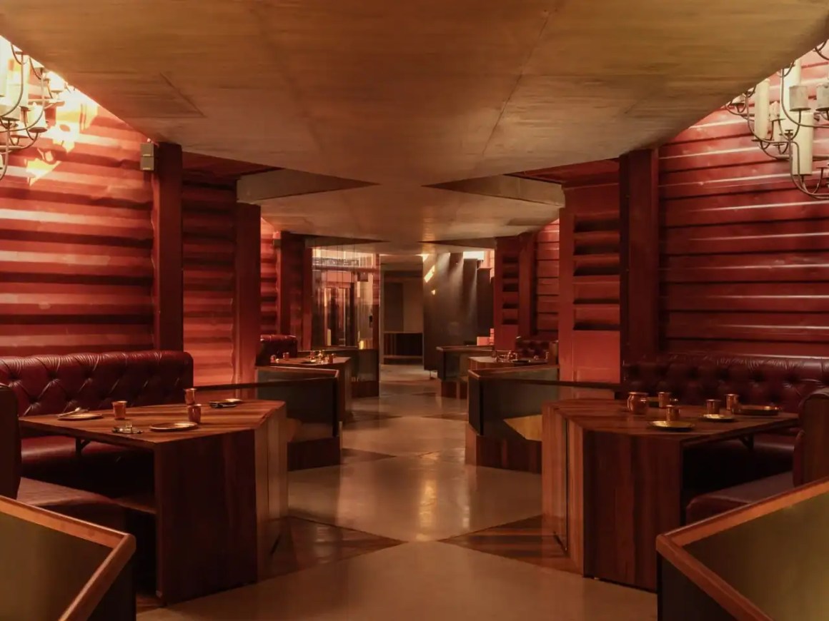 Interior view of a stylish restaurant featuring wooden walls, leather seating, and ambient lighting, with multiple tables set for dining.
